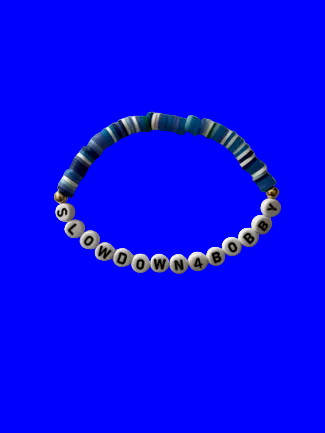 A beaded stretch bracelet,  features blue and white striped beads on one side, a small gold spacer bead, and white letter beads spelling out 'SLOWDOWN4BOBBY'.